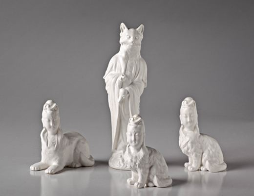 Sculpted white figures of a cat in robes and sphinx like human figures