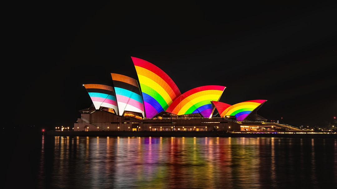 The sails of the Sydney Opera House adorned with the rainbow stripes of the Progress Pride flag.