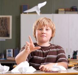 Boy throwing a paper plane in a classroom.
