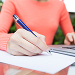 Woman writing on paper with her laptop beside her