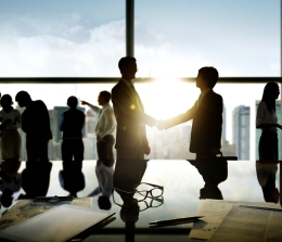 Silhouette of business executives shaking hands with sunset through glass windows 