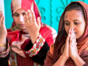 A Muslim woman and a Christian woman both in prayer