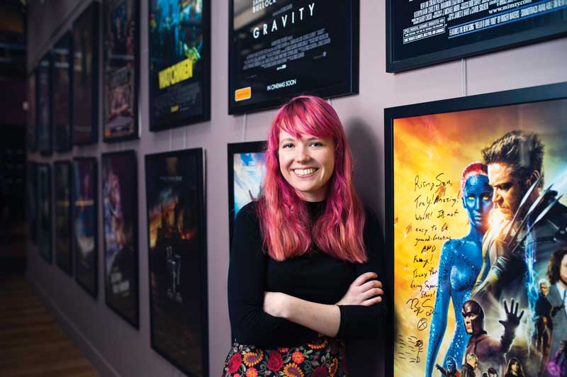 Student smiling in front of film posters at Rising Sun Pictures