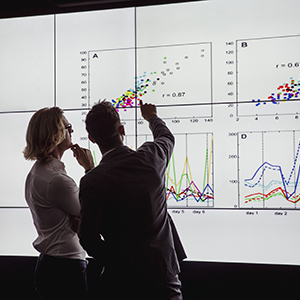 Two people look at data graphs on a large screen