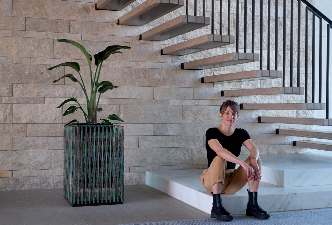 Annika next to The Vessel, a copper and bronze hand-woven sculpture that holds a plant. 