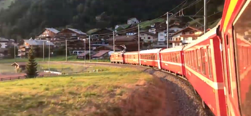 An orange train travelling through a mountain town