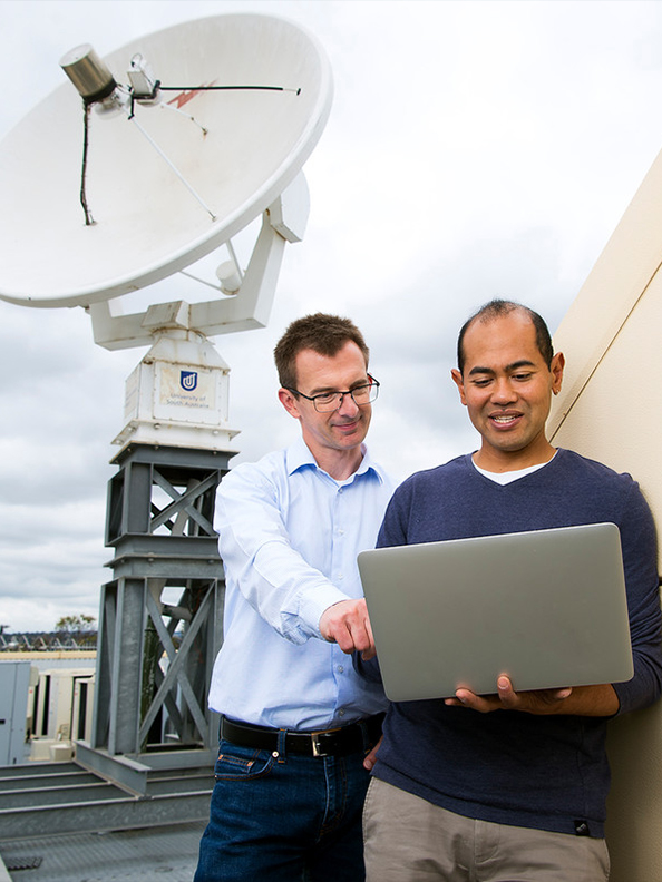 Two researchers working on a laptop with a satellite dish in the background