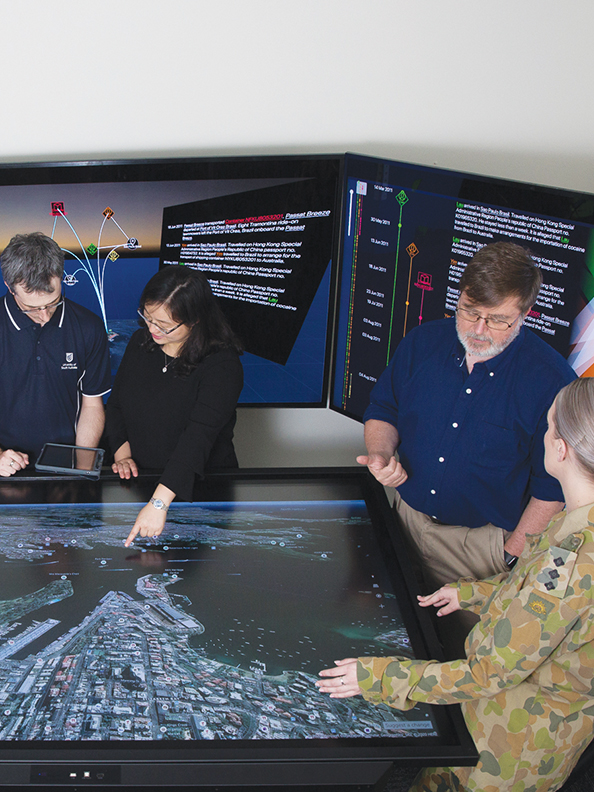 Several people standing around a tabletop monitor displaying an aerial photograph