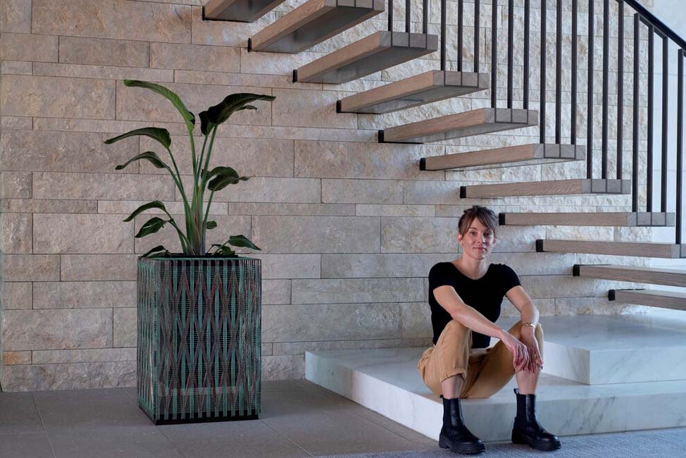 Annika next to The Vessel, a copper and bronze hand-woven sculpture that holds a plant. Source
