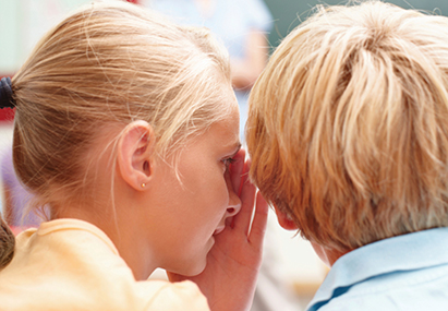 Two school children in the classroom sharing a secret