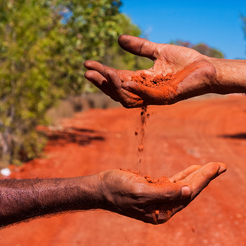 Two hands pouring red dirt