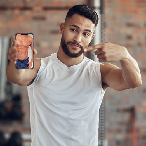 Young man in gym with a picture of the ideal six-pack on his phone