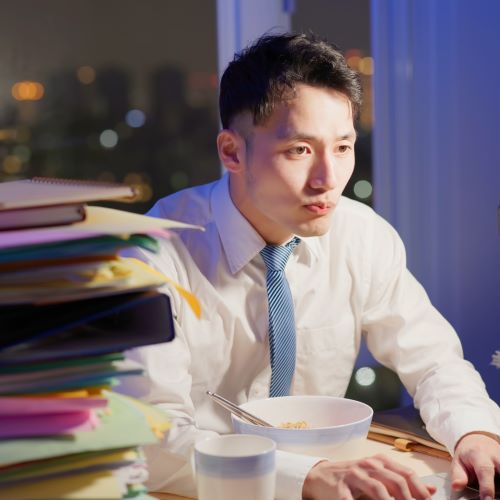 Man eating noodles at his desk while working at night