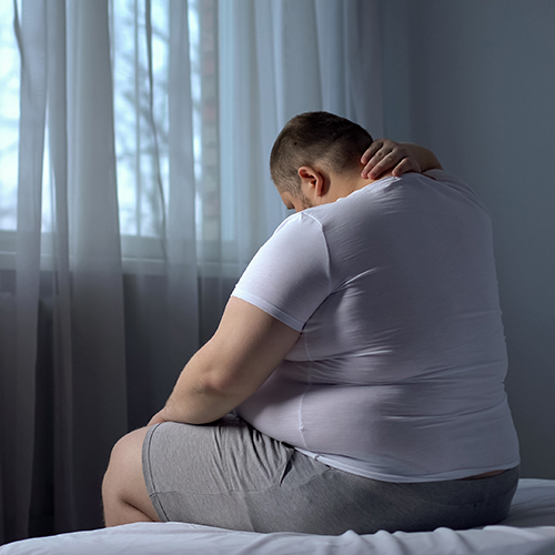 Sad overweight man sitting on the end of his bed