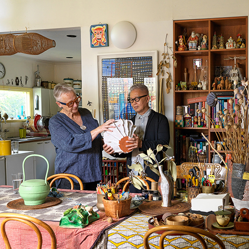 Helen Fuller and Khai Liew stand inside Fuller's home looking at a large ceramic vessel. The house is decorated with many different textiles, artworks and objects that create a riot of pattern, colour and texture.jpg