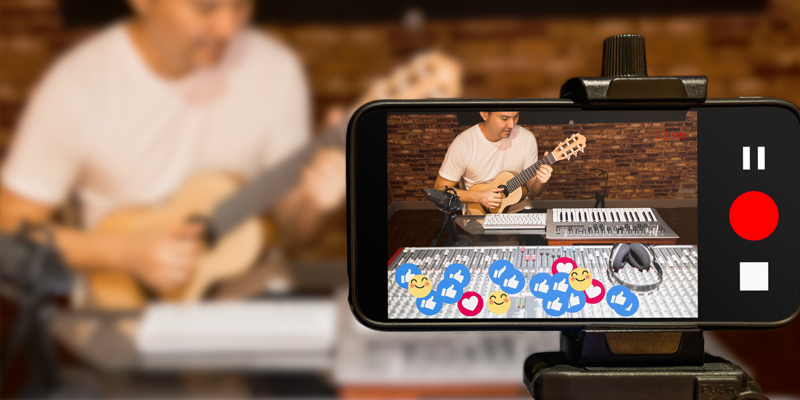 Music vlogger streaming a live video while playing acoustic guitar in home studio. Photo by PrinceOfLove / Shutterstock.com