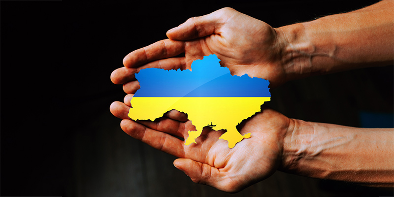 Hands holding the flag of Ukraine in the shape of the borders of Ukraine.
