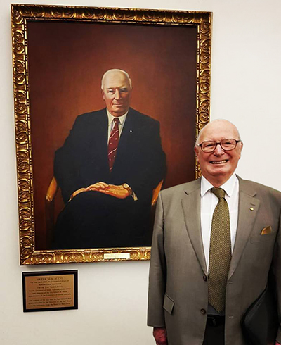 Sir Eric Neal next to his portrait, which is displayed in the Sir Eric Neal Library at UniSA’s Mawson Lakes campus.